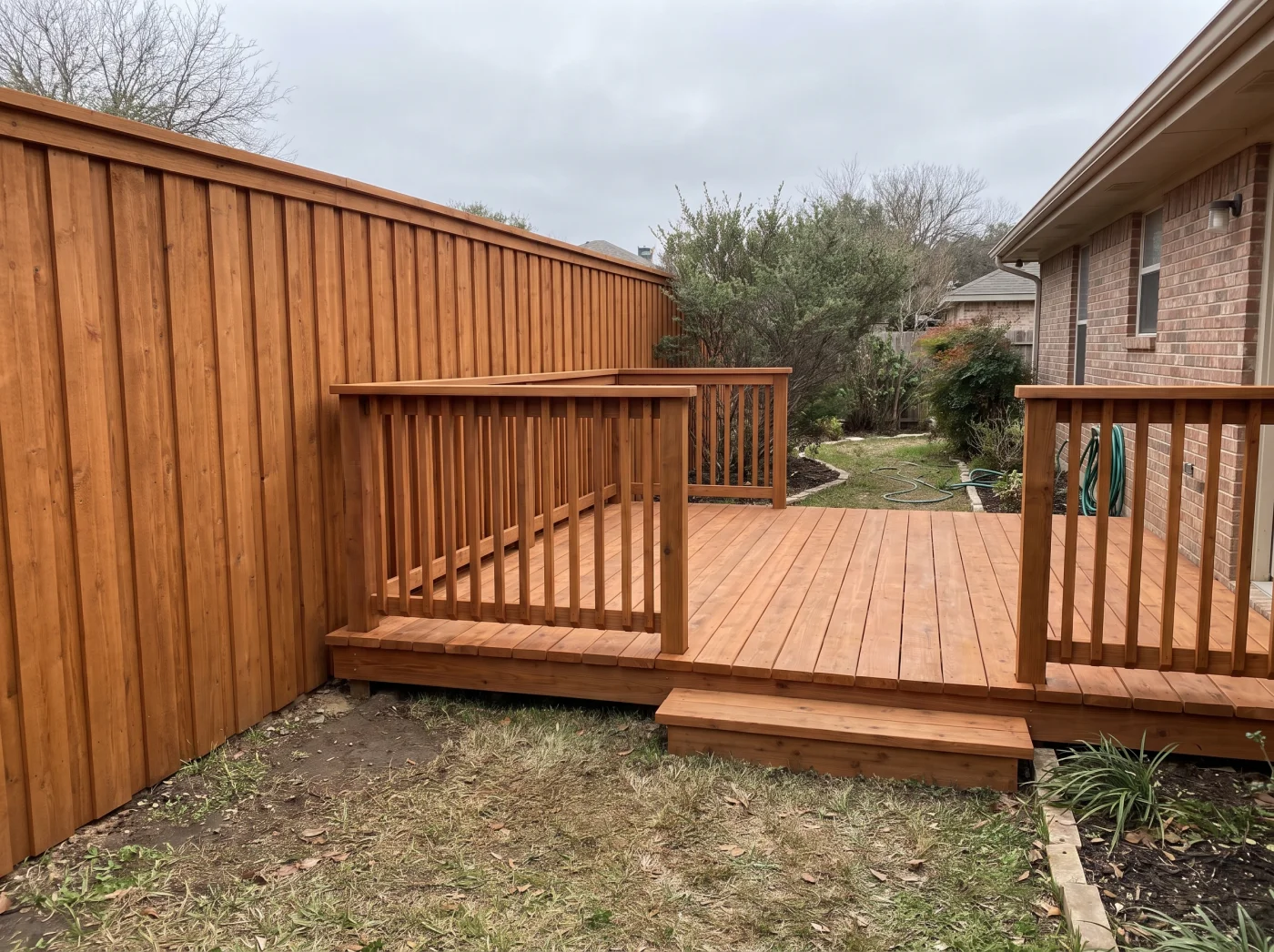 New stained wood deck built into a backyard corner beside a matching cedar privacy fence