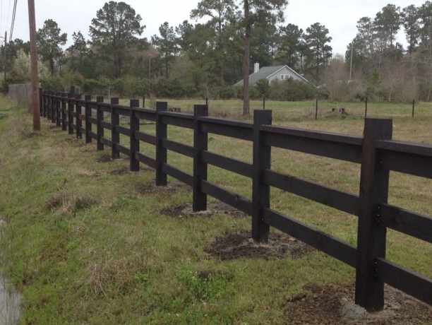Ranch style fence in stained wood rails along an open field