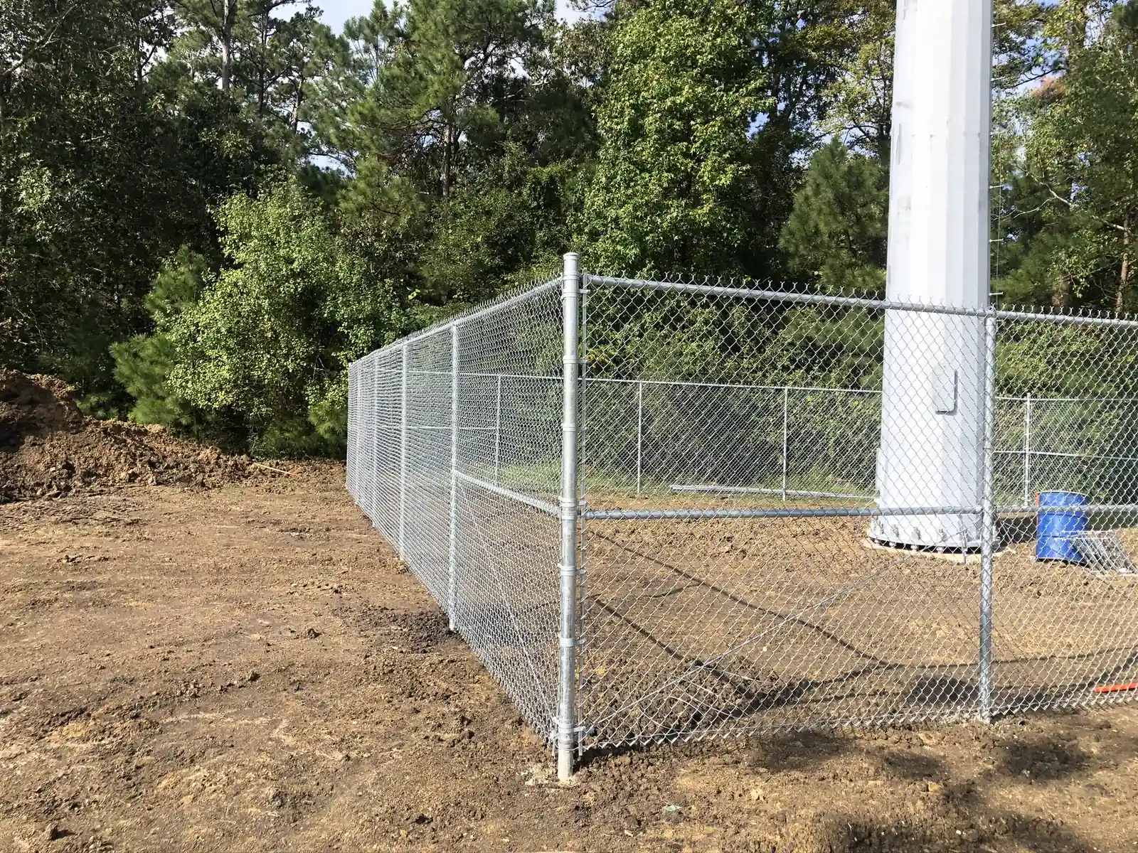 Galvanized chain link fence around a utility tower base near a ball field
