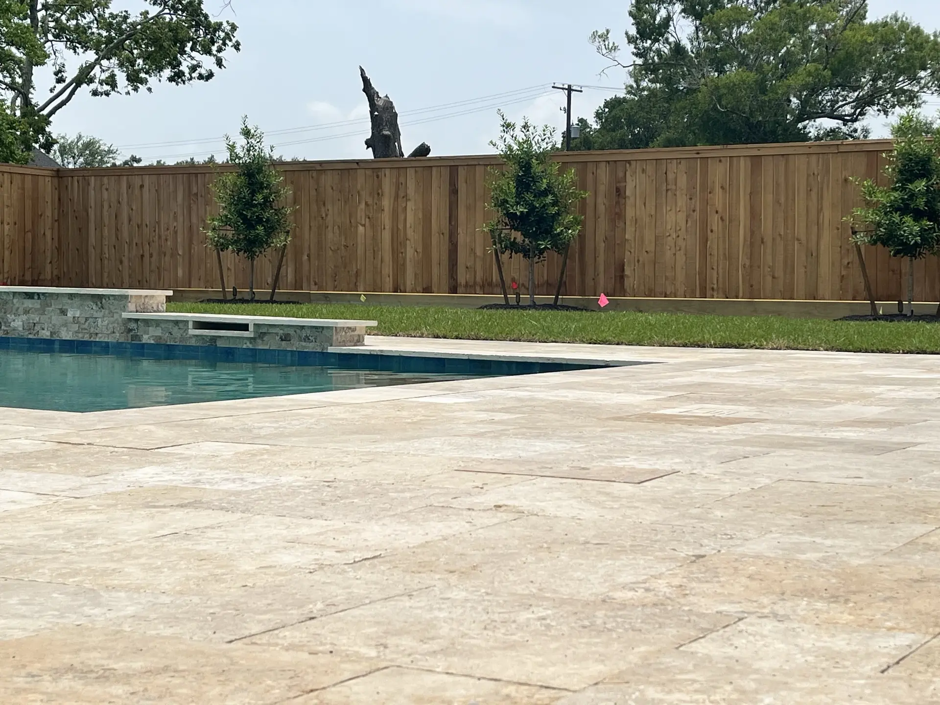 Backyard pool with travertine decking enclosed by a tall wood privacy fence