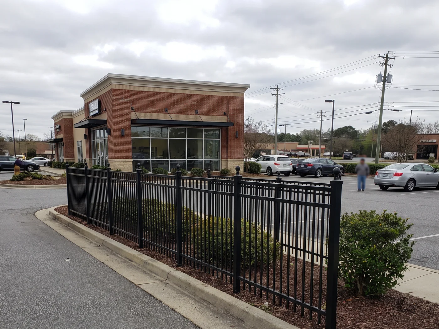 Black aluminum fence along the frontage of a brick retail building