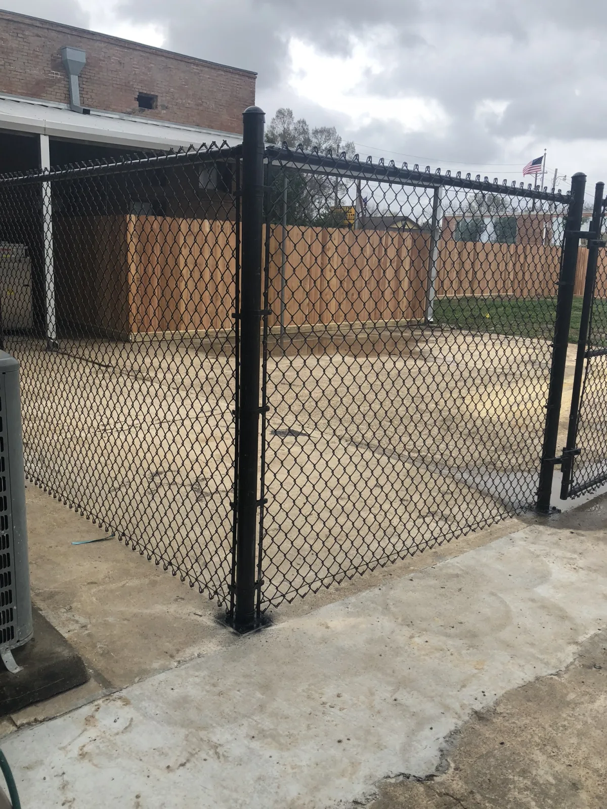 Black chain link commercial fence enclosing a paved lot beside a brick building