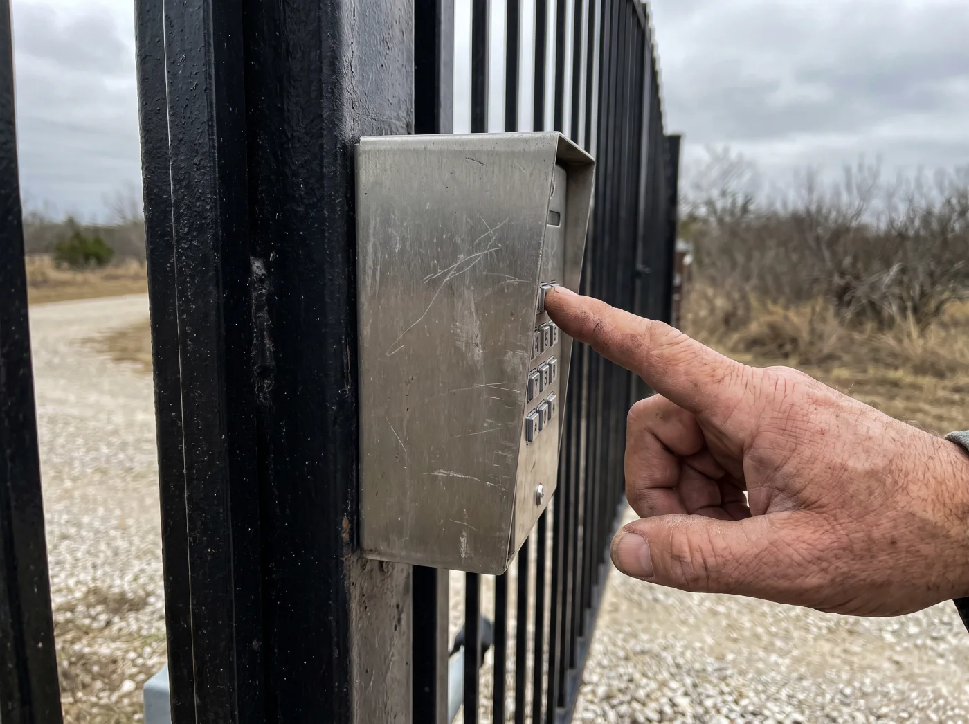 Hand entering a code on a keypad mounted at a driveway gate