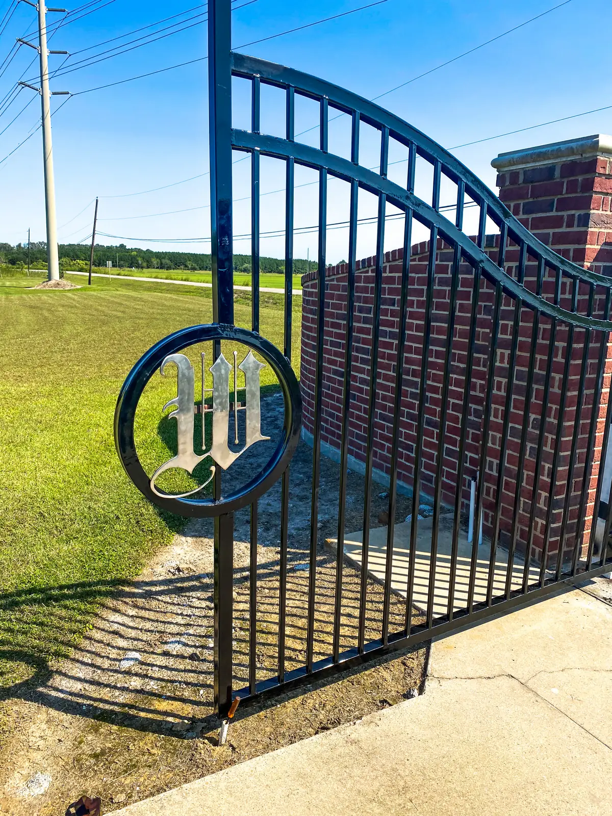 Black wrought iron arched gate with a custom monogram medallion beside a brick column